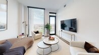Located in the prestigious Forest Hill neighbourhood of Toronto, this refined one-bedroom, one-bathroom residence offers a thoughtfully designed layout that maximizes every square foot. The open-concept living and kitchen area is anchored by warm wide-plank hardwood flooring and an abundance of natural light streaming through dramatic floor-to-ceiling windows, which frame sweeping views of the Toronto skyline and surrounding treetops.

The contemporary kitchen is a standout feature, outfitted with two-tone cabinetry combining white upper cabinets and wood-grain lower units, a sleek stone-topped island with pendant lighting, and high-end integrated appliances. The space flows seamlessly into the living room, where expansive glazing and a private balcony access point invite the outdoors in.

The bedroom is a serene retreat with direct balcony access, large windows, and a built-in sliding-door closet. The bathroom is elegantly finished with large-format marble-look tiles, a soaker tub with a frameless glass sliding enclosure, and a clean white vanity. Throughout the unit, crisp white walls and modern black hardware accents contribute to a polished, cohesive aesthetic. The balcony itself offers unobstructed panoramic views, completing this exceptional urban residence.
