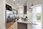 This single-floor residence showcases a thoughtfully designed interior with consistent, contemporary finishes throughout. The kitchen serves as a central highlight, featuring dark gray shaker-style cabinetry, stainless steel appliances including a French door refrigerator, electric range, built-in microwave, and dishwasher. A granite-topped peninsula with pendant lighting provides additional prep space and a casual dining option, while a built-in diagonal wine rack adds a distinctive decorative touch. A textured tile backsplash and light wood-look flooring complete the polished look.

The bedrooms are bright and comfortable, each featuring ceiling fans, natural light from large windows with blinds, and the same warm wood-look flooring that flows throughout the unit. Clean white walls and generous proportions make each room highly adaptable.

The bathrooms are finished to a high standard, with granite countertops, gray shaker vanity cabinetry, brushed nickel hardware, undermount sinks, and large wall mirrors. The primary bathroom includes a dual-sink vanity and a walk-in tiled shower.

A dedicated laundry room houses a full-size top-load washer and dryer with overhead wire shelving for storage. Wide hallways with panel doors connect the spaces seamlessly, contributing to an open, airy ambiance throughout the home.