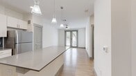 This 630 square foot apartment offers a thoughtful blend of functionality and style. The open-concept design maximizes the use of space, seamlessly integrating the kitchen, living, and dining areas. The kitchen showcases modern white cabinetry, stainless steel appliances, and a sleek gray backsplash, complemented by a central island that doubles as a breakfast bar.

The living area features hardwood flooring and large windows that flood the space with natural light, creating an airy ambiance. A glass door leads to an outdoor area, extending the living space. The bedroom, measuring 150 square feet, is carpeted for comfort and includes a ceiling fan and ample windows for ventilation and light.

The bathroom is efficiently designed with a single vanity, modern fixtures, and continues the hardwood flooring theme. A closet provides additional storage space. Throughout the apartment, recessed lighting and contemporary ceiling fans enhance the overall modern aesthetic.

The neutral color palette, dominated by whites and grays, creates a clean, fresh look that allows for personal decorating preferences. This well-designed one-bedroom apartment offers a perfect balance of comfort and style in a compact urban living space.