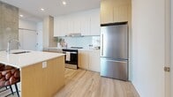 Located at 305 Rue Quinlan in Montréal, this thoughtfully designed one-bedroom, one-bathroom unit offers a well-organized and modern living environment across a single floor. The open-concept layout makes efficient use of the space, creating a bright and airy atmosphere throughout.

The kitchen is a standout feature, showcasing a contemporary design with warm natural wood cabinetry paired with crisp white upper cabinets and a light subway tile backsplash. A generous island with a white quartz countertop provides both additional workspace and casual dining. Stainless steel appliances, including a full-size refrigerator and stainless range, complete the functional yet stylish cooking space. Light hardwood flooring flows throughout, adding warmth and continuity.

The bedroom is a calm and comfortable retreat, benefiting from a large window that invites natural light and offers views of the surrounding neighbourhood. An exposed concrete column adds an industrial character to the otherwise soft, neutral palette of the room.

The bathroom is finished to a high standard, featuring full-height white tiles, a soaker tub with a glass shower panel and handheld showerhead, and warm wood vanity accents that echo the kitchen's design language. Framed artwork adds a refined, curated touch. Overall, the unit presents a cohesive, modern aesthetic with quality finishes throughout.