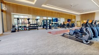 This expansive 2,620 square foot fitness center is a pinnacle of modern exercise facilities. The space boasts an impressive array of cutting-edge equipment, including cardio machines, weight training stations, and specialized workout areas. The layout is thoughtfully designed, with distinct zones for different exercise types, ensuring a smooth flow and comfortable user experience.

The facility's architectural highlights include high ceilings with recessed lighting, creating an open and airy atmosphere. Large floor-to-ceiling windows flood the space with natural light and offer views of the surrounding landscape, enhancing the workout environment. The interior design features a harmonious blend of materials, with warm wood accents contrasting against the sleek, modern exercise equipment.

A striking feature is the vibrant red running track that bisects the space, adding both functionality and visual interest. The floor is covered with high-quality, impact-absorbing material, ideal for various exercise routines. State-of-the-art technology is integrated throughout, with large display screens for guided workouts or entertainment.

The center caters to diverse fitness needs, from cardio enthusiasts to strength training aficionados, making it a comprehensive wellness destination. Its spacious layout, premium equipment, and attention to design details create an inviting and motivating environment for users of all fitness levels.