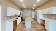 This single-floor unit offers a well-designed layout that balances functionality and modern aesthetics throughout. The kitchen serves as a central highlight, featuring white shaker-style cabinetry, light countertops, and a full suite of stainless steel appliances including a range, microwave, refrigerator, and dishwasher. A center island with pendant lighting above provides additional workspace and casual dining options. The kitchen flows naturally into the surrounding living areas, all finished with durable wood-look plank flooring that carries a warm, cohesive tone throughout the main spaces.

The living area is bright and open, benefiting from natural light admitted through large windows and a glass door that leads to an outdoor access point. Neutral warm-gray wall tones complement the flooring and contribute to a clean, contemporary atmosphere.

The bedrooms are finished with plush carpeting and feature large windows that invite natural light while offering outdoor views. Each bedroom is served by generous closet space, with one room notably equipped with dual side-by-side bi-fold closets, maximizing storage capacity.

The bathroom is finished with the same wood-look flooring found throughout the unit, and includes a full tub-shower combination with a curved rod, white vanity, and clean, neutral finishes that maintain the unit's consistent modern style.