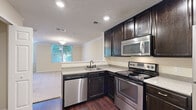 This efficiently designed one-bedroom, one-bathroom residence offers a thoughtful layout across a single floor, making excellent use of every square foot. The open kitchen is a standout feature, showcasing rich dark-stained cabinetry, granite-style countertops, and a full suite of stainless steel appliances including a refrigerator, electric range, built-in microwave, and dishwasher. Dark hardwood-style flooring grounds the kitchen and entry areas, adding warmth and visual contrast. A dedicated closet nook accommodates a stacked washer and dryer, providing the convenience of in-unit laundry. The living area is carpeted and benefits from natural light through large windows framed by lush greenery, creating a bright and inviting atmosphere. Crown molding runs throughout the common areas, lending a refined architectural touch. The bedroom is a comfortable retreat, also carpeted, with a window offering natural light. The bathroom features a wide vanity with a white countertop, dark cabinetry, a large mirror, and hardwood-style flooring. Two closets provide practical storage solutions throughout the residence. Overall, the space presents a clean, neutral palette with quality finishes that balance style and functionality.