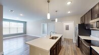 This single-floor residence is designed with a clean, contemporary aesthetic and a thoughtful open-concept layout. The kitchen serves as the centerpiece of the living space, anchored by a large island with a white quartz countertop, an undermount sink, and pendant lighting above. Dark espresso cabinetry lines the walls, providing ample storage, while stainless steel appliances—including a refrigerator, range, microwave, and dishwasher—complete the functional setup. The kitchen flows naturally into the living area, which features wood-look flooring and large windows with a glass door that floods the space with natural light and provides direct outdoor access.

The bedrooms are carpeted for comfort, with ceiling fans and windows offering neighborhood views. The primary bathroom includes a double-sink vanity with quartz countertops, dark cabinetry, wood-look flooring, a walk-in shower, and an adjacent closet with built-in wire shelving. A secondary bathroom features a single vanity and a tub-shower combination. Additional highlights include a dedicated laundry area, a utility panel, and recessed lighting throughout, contributing to the overall bright and polished ambiance of the space.
