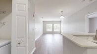 This 2-bedroom, 2-bathroom apartment at Bradlee Danvers in Danvers, MA offers 1,120 square feet of thoughtfully designed living space spread across two floors. The main level encompasses 990 square feet and features an open-concept kitchen and living room area with light wood-tone luxury vinyl plank flooring throughout. The kitchen is equipped with stainless steel appliances, including a refrigerator and range, complemented by dark cabinetry with modern hardware and light countertops. The living room is bright and airy, with large windows fitted with blinds that invite generous natural light and outdoor views of surrounding greenery. Both bedrooms are carpeted and feature neutral gray walls, large windows, and ample natural light. The primary bedroom measures 180 square feet and includes a spacious walk-in closet outfitted with wire shelving and hanging rods for organized storage. A second walk-in closet with similar wire shelving serves the additional bedroom. Each bathroom features wood-tone vinyl plank flooring, a tub-shower combination, and one bathroom includes a white vanity with a framed mirror and stylish lighting. A dedicated entrance and hallway complete the layout. The unit's lower level adds an additional 130 square feet of entry space.