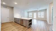 This well-designed two-bedroom, three-bathroom residence in Austin, TX offers a thoughtful open-concept layout filled with contemporary finishes throughout. The kitchen and living area form the heart of the home, centered around a generous island with a white quartz countertop, built-in shelving, a stainless steel sink, and a dishwasher. Gray cabinetry pairs elegantly with stainless steel appliances, including a refrigerator, microwave, and range. Pendant lighting overhead and warm wood-look flooring extending throughout the main living areas create a cohesive, modern aesthetic. The living room benefits from abundant natural light through large windows and a glass door leading to an outdoor area, complemented by a ceiling fan above. Both bedrooms feature plush carpeting, neutral tones, and ample natural light. One bedroom includes a built-in window bench with storage cubbies, adding a charming functional touch. Walk-in closets with multi-tiered shelving and hanging rods provide generous storage. The bathrooms are finished with gray vanity cabinetry, quartz countertops, light tile flooring, and a soaking tub with marble-style tiled surround. A dedicated laundry room houses a stacked full-size washer and dryer unit with additional shelving nearby for added convenience.