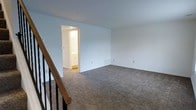 Located at 1741 Lucille Dr in Lima, Ohio, this two-story home offers a straightforward and functional layout spread across two levels. The upper floor features a spacious, open room finished with wall-to-wall carpeting in a neutral tone, providing a comfortable and quiet underfoot feel. The clean white walls throughout lend the space a bright and airy atmosphere, complemented by ample room to accommodate a variety of furniture arrangements. A staircase with a classic wood handrail and dark balusters connects the floors, adding a traditional architectural touch to the interior. Accessible directly from the upper-level room is an adjoining bathroom, visible through a doorway that opens into a well-lit space with cabinetry and tiled flooring, offering convenient access from the main living area. The overall design is clean and understated, with a neutral color palette that creates a versatile backdrop suitable for a range of interior styles. The home's two-floor configuration provides natural separation between living spaces, supporting both privacy and functionality throughout the residence.