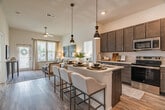 Located in Collierville, TN, this single-story, 2-bedroom, 2-bathroom home offers a thoughtfully designed open-concept layout with modern finishes throughout. The kitchen is a standout feature, showcasing rich dark taupe cabinetry extending to the ceiling, stainless steel appliances, light countertops, and a large center island with seating for multiple guests — all illuminated by sleek pendant lighting. Light wood-look flooring flows seamlessly from the kitchen into the living area, which benefits from soaring ceilings, a ceiling fan, and a glass door that invites natural light and outdoor views. The primary bedroom provides a comfortable retreat with plush carpeting, generous natural light from wide windows, and a well-sized closet. The second bedroom mirrors this bright, airy feel. Both bathrooms are finished with dark cabinetry, white countertops, wood-look flooring, and glass-enclosed showers. A dedicated laundry room with side-by-side full-size washer and dryer adds everyday convenience. Two closets provide ample storage throughout the home. The overall ambiance is clean, modern, and welcoming — a practical yet stylish residence in the heart of Collierville.