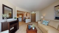Located at 4835 Easy St in Delafield, Wisconsin, this single-floor unit offers a thoughtfully designed open-concept layout that connects the main living and functional areas seamlessly. The living room is a comfortable, well-lit space featuring a large window with vertical blinds that allows natural light to fill the room, complemented by neutral carpet flooring and warm beige tones throughout. A half-wall partition elegantly separates the living area from the entry foyer and kitchen, creating defined zones while maintaining an open, airy feel. The kitchen is equipped with warm wood cabinetry extending to the ceiling for ample storage, a white range, black dishwasher, and a refrigerator. Tile flooring runs through the kitchen and dining nook, which offers a cozy spot for everyday meals. Adjacent to the entry, a closet area provides convenient storage. A dedicated office or flex room features carpeted flooring and enough space to accommodate a full desk setup, making it ideal for working from home or use as an additional room. The bathroom is finished with tile wainscoting, stone-look tile flooring, a wood vanity with a single sink, and a medicine cabinet above. The overall palette of warm neutrals and natural wood tones gives the unit a cohesive and inviting character throughout.