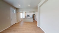 Located at 5811 102nd Street in Lubbock, Texas, this single-story home offers a clean, modern aesthetic defined by an open-concept floor plan and thoughtfully selected finishes. The living and kitchen areas flow seamlessly into one another, connected by a graceful arched passageway that adds architectural character to the space. Warm, light-toned hardwood flooring runs throughout, lending a sense of continuity and brightness to every room. The kitchen serves as a functional centerpiece, featuring crisp white cabinetry, a tiled backsplash, dark countertops, and stainless steel appliances including a refrigerator and built-in microwave. A central island with bar-height seating provides additional prep space and a natural gathering point. Recessed lighting in the kitchen ensures well-distributed illumination, complementing the natural light that filters in through the windows. The neutral color palette of soft whites and warm beige tones throughout the interior creates a calm, inviting atmosphere. The entry features a classic craftsman-style front door, offering a welcoming first impression. Overall, the space strikes a balance between contemporary design and everyday comfort, making it a well-appointed and move-in ready home.