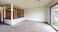 Located at 4301 Lincoln Swing in Ames, Iowa, this single-floor unit offers a practical and efficiently laid-out living space. The living room is carpeted in a neutral tone and bathed in natural light, thanks to a large sliding glass door that opens onto a private balcony. The balcony overlooks a green, tree-lined yard, providing a pleasant outdoor retreat. A ceiling fan is centrally positioned above the living area, contributing to both comfort and airflow. A distinctive decorative wood spindle railing with warm-toned trim serves as an architectural divider, adding visual interest and a classic character to the space. Adjacent to the living room, the kitchen features dark wood cabinetry, a white range, and tile flooring, offering a functional cooking area. The bathroom is clean and well-appointed, with a wood-toned vanity, an integrated white countertop and sink, and a mirrored medicine cabinet above. Warm wood trim is carried consistently throughout the unit, lending a cohesive and traditional aesthetic. The overall layout is compact yet thoughtfully organized, making efficient use of every square foot available.