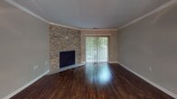 This single-story space is thoughtfully designed with a cohesive neutral color palette and a mix of hardwood flooring and plush carpeting throughout. The living room serves as a central focal point, showcasing rich, dark hardwood floors, crown molding, and a striking stacked-stone fireplace that extends to the ceiling. A large sliding glass door with vertical blinds fills the room with natural light and provides direct outdoor access to a greenery-lined exterior. An adjacent area features a ceiling fan and additional hardwood flooring, offering flexible living space.

The kitchen is well-appointed with white shaker-style cabinetry, dark countertops, a subway tile backsplash, and a stainless steel sink, creating a clean and functional layout. The bedrooms are carpeted and neutrally toned; one features a sliding-door closet, while another includes a sliding glass door opening to an outdoor patio with brick detailing and wooded views. The bathrooms are finished with white vanity cabinetry, dark countertops, and wood-look flooring, maintaining a consistent modern aesthetic throughout the space.