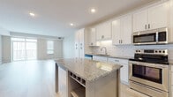 This single-floor unit is designed with a clean, contemporary aesthetic throughout. The open-concept kitchen and living area serves as the focal point of the space, featuring white shaker-style cabinetry extending to the ceiling, granite countertops, and a classic white subway tile backsplash. A central kitchen island with a matching granite surface includes built-in wine storage and open shelving below, providing both functionality and style. Stainless steel appliances, including a French door refrigerator, range, microwave, and dishwasher, complete the kitchen. Light hardwood-style flooring flows throughout the main living areas, enhancing the bright, airy atmosphere created by recessed lighting and natural light from windows.

The bedrooms feature plush carpeting and windows with blinds. The bathrooms are finished consistently with granite-topped white vanities, matte black hardware, large mirrors, and light wood-style flooring. One bathroom includes a tub-shower combination, while another features an elongated vanity layout. A dedicated laundry room with a full-size washer and dryer and wall-mounted shelving adds everyday convenience to this well-appointed space.