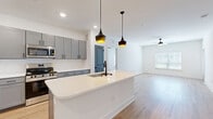 This well-appointed 2-bedroom, 2-bathroom residence offers a thoughtfully designed single-floor layout with a clean, modern aesthetic. Light wood flooring runs throughout the entire space, creating a warm and cohesive feel from room to room.

The open-concept kitchen and living area serves as the heart of the home. The kitchen features a large central island with a white quartz countertop and undermount sink with a matte black faucet, complemented by gray shaker-style cabinetry, stainless steel appliances, and stylish pendant lighting. A built-in wine rack adds a distinctive touch. The kitchen flows seamlessly into a spacious living area illuminated by natural light from a large window and equipped with a ceiling fan.

Both bedrooms are generously sized, each featuring ceiling fans, large windows with blinds, and white walls that enhance the bright, airy atmosphere. The primary bedroom connects to a private en-suite bathroom with a dual-sink gray vanity, white quartz countertops, matte black fixtures, and a marble-tiled walk-in shower. The second bathroom features a full soaking tub with marble-tiled surround. Two well-organized closets with built-in wire shelving provide ample storage throughout the home.