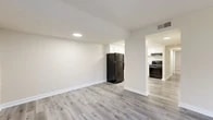 This thoughtfully designed one-bedroom, one-bathroom residence offers a functional and modern living environment across a single floor. The open living room serves as the heart of the unit, featuring light gray luxury vinyl plank flooring, warm neutral-toned walls, and two windows alongside a glass sliding door that invites natural light and provides views of the surrounding greenery. The space flows naturally into the kitchen and dining area, where black appliances—including a refrigerator, gas range, and dishwasher—contrast cleanly against white shaker-style cabinetry and light granite countertops. Recessed and flush-mount lighting keeps the kitchen bright and practical.

The bedroom is carpeted in a soft gray tone, offering a comfortable retreat with a dedicated closet and a window dressed with vertical blinds overlooking the outdoors. Direct access to the bathroom is conveniently positioned nearby. The bathroom is finished with marble-style floor and shower tile, a soaking tub, a gray vanity with a white countertop, and a well-lit mirror above. Clean white trim and baseboards are consistent throughout, contributing to a cohesive, well-maintained aesthetic across the entire unit.