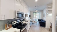 Located on E 7th Street in the heart of East Austin, this efficiently designed one-bedroom, one-bathroom unit offers a thoughtful layout that maximizes every square foot. Light wood-look flooring runs throughout, creating a cohesive and contemporary feel across the single floor.

The open-plan kitchen and living area form the core of the space. The kitchen is outfitted with white shaker-style cabinetry extending to the ceiling, a tiled backsplash, white quartz countertops, and a full suite of stainless steel appliances including a range, over-the-range microwave, dishwasher, and refrigerator. The living area flows naturally from the kitchen and is anchored by a sliding glass door that brings in natural light and connects to an outdoor view, complemented by a ceiling fan overhead.

The bedroom is a cozy, well-appointed retreat featuring warm neutral walls, dark curtain panels that allow for light control, wood-look flooring, and a full-length mirror. The bathroom is clean and functional, finished with tiled walls in the shower-tub combo, white cabinetry for storage, and a small window for natural ventilation. The overall ambiance of the unit is modern and understated, with a neutral palette that lends itself well to the vibrant East Austin neighborhood surrounding it.
