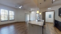 This single-floor residence offers a thoughtfully designed open-concept layout that seamlessly connects the kitchen, dining, and living areas. Rich, dark hardwood-style flooring runs throughout the main living spaces, creating a warm and contemporary atmosphere complemented by tall ceilings and ceiling fans that enhance the sense of openness.

The kitchen is a standout feature, equipped with dark espresso cabinetry extending to the upper walls, granite-style countertops, and a full suite of stainless steel appliances including a refrigerator, electric range, and built-in microwave. A mosaic tile backsplash adds texture and visual interest. A peninsula island with an integrated sink and pendant lighting above serves as a natural dividing point between the kitchen and the expansive living area, which receives natural light through sliding glass doors leading to an exterior access point.

The bedroom features plush carpeting, a ceiling fan, and multiple windows fitted with blinds that allow natural light while maintaining privacy. An adjoining walk-in closet offers wire shelving for organized storage. The unit also includes a dedicated laundry room housing a full-sized washer and dryer with overhead shelving, adding practical convenience to everyday living.