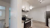 This single-floor unit showcases a clean, modern aesthetic carried consistently throughout its layout. The kitchen serves as a functional centerpiece, designed in a galley style with white shaker cabinetry, brushed nickel hardware, and dark gray countertops that provide a crisp contrast. Stainless steel appliances — including a range with an overhead vent hood, a dishwasher, and a refrigerator — complete the well-equipped space, which is finished with wood-look flooring and flush ceiling lighting.

The living area is bright and open, benefiting from natural light that enters through a sliding glass door leading to a balcony with exterior views. Crown molding frames the ceiling, adding a refined architectural detail to the otherwise clean-lined space. Wood-look flooring continues seamlessly from the kitchen through the living and bedroom areas, providing visual cohesion.

The bedroom offers natural light through a large window with vertical blinds, a ceiling fan, and access to a dedicated closet with built-in shelving. The bathroom features a full tub-shower combination, a vanity with an integrated sink, and wood-look flooring consistent with the rest of the unit.