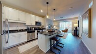 This well-designed single-floor residence offers a seamless blend of modern finishes and functional living spaces. The open-concept kitchen is a standout feature, outfitted with crisp white shaker cabinetry, dark granite countertops, a classic subway tile backsplash, and a full suite of stainless steel appliances including a refrigerator, range, microwave, and dishwasher. A central island with bar seating and stylish pendant lighting makes the kitchen an ideal hub for both cooking and casual dining. The kitchen flows naturally into the living area, which is bright and welcoming, benefiting from a large sliding glass door that opens to an outdoor balcony and allows generous natural light to fill the space. Wood-style flooring runs throughout the main living areas, adding warmth and continuity. The bedroom is a comfortable retreat, featuring plush carpeting, a closet, and a window with views to the exterior. The bathroom is clean and well-finished with wood-look tile flooring and crisp white fixtures. A dedicated in-unit laundry room provides added convenience, complete with a full-size washer and dryer alongside extensive wire shelving for storage. Overall, the space presents a cohesive, contemporary aesthetic with practical amenities throughout.