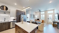 Located at 3811 Commerce Way in Sacramento, CA, this well-appointed 2-bedroom, 2-bathroom residence offers a thoughtfully designed single-level layout. The bright living room features light hardwood-style flooring, a ceiling fan, floor-to-ceiling drapes, and a private balcony access door that floods the space with natural light and outdoor views. The kitchen is a standout, showcasing a two-tone cabinetry design with white upper cabinets and dark wood lower cabinets, white quartz countertops, a textured tile backsplash, open shelving, stainless steel appliances, and matte black fixtures. A central island provides additional prep and storage space. The spacious primary bedroom benefits from large windows with exterior views, plush carpet flooring, a ceiling fan, a walk-in closet, and a wall-mounted TV. The en suite bathroom features a dual-sink vanity with dark wood cabinetry, white countertops, and light hardwood-style flooring. The second bedroom is equally comfortable with ample natural light and closet access. The guest bathroom includes a wood-tone vanity, a tub-shower combination, and matte black accents. Neutral tones and modern finishes carry throughout, creating a cohesive, contemporary ambiance.