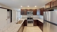 This single-floor unit offers a well-designed, open-concept layout that seamlessly connects the kitchen and living areas. The kitchen serves as a central highlight, featuring rich dark-stained cabinetry with brushed nickel hardware, light granite countertops, and a full suite of stainless steel appliances, including a range, over-the-range microwave, and refrigerator. A kitchen island with a double undermount sink provides additional workspace and casual dining potential. Recessed lighting illuminates the kitchen, enhancing its polished appearance. Light wood-style flooring runs throughout the unit, creating a cohesive and contemporary feel. The open living area is generously proportioned, benefiting from large windows that invite natural light and outdoor views. A ceiling fan with an integrated light fixture adds comfort and functionality to one of the rooms. The bathroom is neatly appointed with a dark-stained vanity, granite-style countertop, a large wall mirror, and a full tub-shower combination with a curved curtain rod. Light wood-style flooring continues into the bathroom, maintaining consistency throughout the unit. Overall, the space presents a clean, modern aesthetic with practical finishes.
