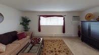 Located at 2294 Zink Rd. in Fairborn, Ohio, this single-floor unit offers a functional and comfortable layout across several well-defined living spaces. The living room provides a welcoming atmosphere with soft carpeting, a large window dressed with decorative drapes that allow natural light to fill the room, and a wall-mounted air conditioning unit. Baseboard heating runs along the walls, ensuring year-round comfort. The kitchen is efficiently designed with ample upper and lower cabinetry in a two-tone dark and white finish, a double-basin sink, a dishwasher, and a coil-top electric range and oven. Tile flooring and an adjacent dining area make this a practical space for everyday use. The primary bedroom is generously sized with carpeted floors, a window with curtain panels, baseboard heating, and room for a seating area. A second bedroom offers similar carpeted comfort and features a wide sliding-door closet with built-in shelving, providing notable storage capacity. The full bathroom is finished with light tile flooring, a single-sink vanity with under-sink cabinetry, a lighted mirror cabinet, and a shower-tub combination with a curtain enclosure. Overall, the unit presents a straightforward, practical living environment suited for comfortable day-to-day living.