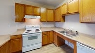 Located at 1145 Hudson Rd in Saint Paul, Minnesota, this single-floor unit offers a practical and well-organized layout throughout. The kitchen is a standout feature, equipped with warm oak cabinetry, ample upper and lower storage, light countertops, a white electric range, dishwasher, full-size refrigerator, and a stainless steel sink. A peninsula with an extended countertop provides additional workspace and separates the kitchen from the adjoining area. Light wood-style flooring runs through the kitchen and living spaces, lending a clean, cohesive look. The open living area receives natural light through dual windows, creating a bright and welcoming atmosphere, while a pendant light fixture adds a decorative touch overhead. A hallway connects the main living spaces to the private areas of the unit. The bedrooms feature neutral-toned carpet, warm beige walls, and windows that allow natural light in, with baseboard heating ensuring comfort year-round. The bathroom is designed with accessibility in mind, featuring grab bars near the walk-in shower and toilet, a wood-trimmed vanity with a mirror, and light wood-style flooring. Textured ceilings and warm wood trim details are consistent throughout, giving the unit a cohesive and functional character.