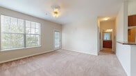 This single-floor residence at 9001 SR-21 S in Port Wentworth, Georgia, offers a straightforward and functional layout designed for comfortable everyday living. The entryway features tile flooring that transitions into plush wall-to-wall carpeting throughout the main living areas and bedrooms, creating a warm and cohesive aesthetic.

The spacious living area is bathed in natural light through large windows and a glass-paneled exterior door, offering pleasant outdoor views of surrounding greenery. The neutral beige walls and soft carpeting lend a calm, understated ambiance to the space. A decorative ceiling light fixture adds a subtle accent overhead.

The kitchen is equipped with warm-toned wood cabinetry, granite-style countertops, and black appliances including a gas range, refrigerator with ice dispenser, and built-in microwave. Open corner shelving adds both storage and visual interest, while a peninsula counter creates a natural division between the kitchen and adjacent living area. Tile flooring runs throughout the kitchen for easy maintenance.

The bathroom features rich wood cabinetry paired with dark granite-style countertops, a large vanity mirror, tile flooring, and a full tub-shower combination. A bedroom includes sliding glass door access to an outdoor area, vertical blinds, and a connected walk-in closet, completing this well-organized unit.