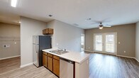 This single-story residence on Tranquility Drive in Rossville, Georgia, is designed with an open-concept layout that promotes a sense of spaciousness and easy flow between living areas. The kitchen serves as a central hub, featuring warm wood-toned cabinetry, light countertops, and a full suite of stainless steel appliances including a refrigerator, electric range with microwave, and dishwasher. A peninsula with an integrated sink separates the kitchen from the adjacent dining and living areas, providing both additional workspace and a natural gathering point.

The living area is finished with light-toned luxury vinyl plank flooring that extends throughout the main living spaces, complementing the neutral gray wall tones. A set of French doors floods the space with natural light and provides outdoor access, while a ceiling fan enhances comfort. The open sightlines from the kitchen through to the living area create a cohesive, airy atmosphere.

The bedrooms are carpeted for comfort and each include ceiling fans. At least one bedroom features direct access to a private bathroom, complete with warm wood vanity cabinetry. Windows in the bedrooms allow natural light while maintaining privacy. Overall, the unit offers a clean, functional design well-suited for comfortable everyday living.