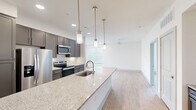 This single-story, 3-bedroom, 2-bathroom home features a modern open-concept design that seamlessly connects the kitchen and living area. The kitchen is a standout, showcasing dark gray cabinetry, a white subway tile backsplash, stainless steel appliances, and a large granite-topped island with an undermount sink and stylish pendant lighting — ideal for both cooking and casual dining. Light wood-look flooring runs throughout the main living areas, enhancing the bright, airy atmosphere complemented by recessed lighting and a ceiling fan.

The primary bedroom is a generously sized retreat with plush carpeting, a ceiling fan, and direct access to an en-suite bathroom. The bathrooms are finished with granite countertops, tile flooring, and clean white cabinetry, with one featuring a soaking tub and tiled surround. The additional bedrooms are well-proportioned with carpeted floors and natural light from blinds-covered windows.

Storage is well-addressed with two dedicated closets, including a walk-in closet with multi-level shelving and hanging rods. A dedicated laundry room houses a full-size side-by-side washer and dryer. The overall design balances contemporary aesthetics with practical functionality throughout.