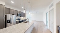 This single-story, 3-bedroom, 2-bathroom home features a modern open-concept design that seamlessly connects the kitchen and living area. The kitchen is a standout, showcasing dark gray cabinetry, a white subway tile backsplash, stainless steel appliances, and a large granite-topped island with an undermount sink and stylish pendant lighting — ideal for both cooking and casual dining. Light wood-look flooring runs throughout the main living areas, enhancing the bright, airy atmosphere complemented by recessed lighting and a ceiling fan.

The primary bedroom is a generously sized retreat with plush carpeting, a ceiling fan, and direct access to an en-suite bathroom. The bathrooms are finished with granite countertops, tile flooring, and clean white cabinetry, with one featuring a soaking tub and tiled surround. The additional bedrooms are well-proportioned with carpeted floors and natural light from blinds-covered windows.

Storage is well-addressed with two dedicated closets, including a walk-in closet with multi-level shelving and hanging rods. A dedicated laundry room houses a full-size side-by-side washer and dryer. The overall design balances contemporary aesthetics with practical functionality throughout.