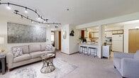 Located at Foxhaven Run in Waukesha, Wisconsin, this single-floor 1-bedroom, 1-bathroom residence offers a practical and comfortable layout designed for efficient everyday living. The open-concept living and kitchen area serves as the heart of the home, where a spacious carpeted living room is illuminated by a striking curved track lighting system overhead. A pass-through breakfast bar with seating connects the living area to the kitchen, which features cream cabinetry with wood-tone accents, tile flooring, and a full suite of appliances including a dishwasher, range, and refrigerator. A dedicated dining nook with a bistro-style table and a closet provides additional functionality near the kitchen. The bedroom offers a comfortable retreat with soft carpeting, a wood-framed window that brings in natural light, and mirrored sliding closet doors that enhance the sense of space. The full bathroom is finished with tile flooring, an extended vanity with ample counter space, a large mirror, and a shower-tub combination. A hallway connects all areas seamlessly, and a separate entry area with natural light and workspace potential rounds out this thoughtfully arranged residence.