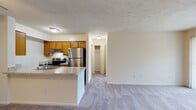 This single-floor residence offers a practical and comfortable layout designed for easy everyday living. The open-concept living and dining area is finished with plush wall-to-wall carpeting and features a ceiling fan, providing a warm and inviting atmosphere. A front entry door with a tile foyer transitions seamlessly into the carpeted main living space.

The kitchen is positioned adjacent to the living area and is defined by a peninsula counter with a granite-style surface, offering convenient bar-style seating and a built-in sink. Warm honey-toned cabinetry lines the walls, providing ample storage, while stainless steel appliances — including a refrigerator and electric range — complete the functional cooking space.

A hallway off the main living area leads to the bedroom and a walk-in closet, offering generous storage. The bedroom is carpeted, spacious, and features a large sliding glass door with vertical blinds that fills the room with natural light and provides direct access to an outdoor area.

The bathroom is well-appointed with wood-look vinyl flooring, a single-sink vanity with warm wood cabinetry and a white countertop, a large mirror, and a shower-tub combination. Clean white walls and chrome fixtures contribute to a crisp, tidy aesthetic throughout the space.