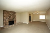 This single-floor residence offers a practical and comfortable layout across several well-defined living spaces. The living room serves as a central gathering area, highlighted by a striking floor-to-ceiling brick fireplace that anchors the room with a classic, rustic charm. Plush carpeting extends throughout the living area, adding warmth underfoot, while a sliding glass door invites natural light and provides access to an outdoor space. A ceiling fan adds to the comfort of the space.

The kitchen is well-appointed with warm wood cabinetry, light granite-style countertops, and black appliances including an electric range with overhead ventilation. Wood-look flooring runs through the kitchen, complementing the cabinetry tones and providing a durable, easy-to-maintain surface.

The bedroom is generously sized with soft carpeting, neutral wall tones, and a textured ceiling. A built-in closet with rod and shelving provides practical storage, and a window allows natural light to brighten the room.

The bathroom features wood-look flooring, a vanity with granite-style countertops, warm wood cabinetry, and access to an additional closet or storage space. Neutral tones throughout the unit create a cohesive, move-in-ready aesthetic.
