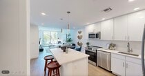 Located at 1950 Mayfair St in Naples, Florida, this thoughtfully designed one-bedroom, one-bathroom residence offers a clean, contemporary aesthetic throughout its efficiently utilized single-floor layout. Light wood flooring and crisp white walls create a bright, airy atmosphere that flows seamlessly from room to room.

The open-concept kitchen is a standout feature, showcasing high-gloss white cabinetry, a herringbone-tiled backsplash, quartz countertops, and a full suite of stainless steel appliances including a range, microwave, and French door refrigerator. A central island with pendant lighting and bar seating connects the kitchen directly to the dining and living areas, making it ideal for both everyday living and entertaining.

The living room is bathed in natural light from large sliding glass doors that open to a private balcony, offering lush views of swaying palm trees. The bedroom is a comfortable retreat, featuring a bright window with outdoor views, a ceiling fan, and a dedicated closet. In-unit laundry adds everyday convenience.

The bathroom is finished with white cabinetry, a quartz vanity, an illuminated mirror, and a tub-shower combination. The overall design is modern and cohesive, with a coastal-inspired palette perfectly suited to the Naples, FL lifestyle.