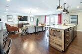 Located at 1900 Rice Mine Rd N in Tuscaloosa, Alabama, this single-floor space offers a thoughtfully designed interior with a cohesive modern-rustic aesthetic. Rich dark hardwood flooring flows throughout, complemented by crown molding, textured ceilings, and neutral warm-toned walls that create a welcoming and polished atmosphere.

The kitchen is a standout feature, equipped with stainless steel appliances including a French door refrigerator, electric range with a sleek stainless steel wall-mounted hood, and a full subway tile backsplash extending to the ceiling. Dark wood cabinetry pairs elegantly with light granite countertops, and a large kitchen island with bar seating provides additional workspace and casual dining.

Adjacent to the kitchen, a dedicated dining area accommodates a substantial rustic wood dining table with industrial-style metal chairs, positioned near a window that invites natural light. The living area is generously sized, featuring a large wall-mounted flat-screen television, a sectional sofa, and leather accent chairs arranged on a chevron-patterned area rug. A secondary seating area includes a standing desk workspace and additional leather chairs.

A reception or waiting area near the entrance features a reclaimed wood accent wall, framed artwork, and additional seating, adding character and visual interest. Throughout the space, recessed lighting and in-ceiling speakers enhance both functionality and ambiance.