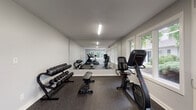Located at 4365 Bayshire Rd in Groveport, Ohio, this single-floor fitness center is a well-equipped and thoughtfully designed workout facility. The space features a long, open layout that maximizes functionality and ease of movement between exercise zones. Durable rubber flooring with a speckled finish covers the entire area, providing both safety and comfort underfoot. Overhead fluorescent lighting ensures consistent illumination throughout the facility, complemented by an abundance of natural light streaming in through a generous row of large windows lining one wall. These windows offer pleasant views of the surrounding greenery, creating an inviting and energizing atmosphere. The cardio zone is outfitted with Star Trac treadmills, an elliptical trainer, and a stationary upright bike, catering to a variety of aerobic workout preferences. A rowing machine adds further versatility to the cardio offerings. The strength training area features a multi-tiered dumbbell rack stocked with a full range of free weights, accompanied by an adjustable workout bench. A mirrored wall enhances the sense of space while allowing users to monitor their form. Sanitation supplies are conveniently stationed within the facility, promoting cleanliness and hygiene. Direct exterior access via a glass-paneled door adds convenience for users.