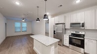 This well-designed 2-bedroom, 2-bathroom residence features a thoughtful single-level layout that maximizes functionality and style. The open-concept kitchen and living area serves as the heart of the home, anchored by a central granite-topped island illuminated by two sleek pendant lights. The kitchen is outfitted with light wood cabinetry, stainless steel appliances including a French door refrigerator, electric range, built-in microwave, and dishwasher, all set against a clean tile backsplash. Wood-look flooring flows throughout the main living areas, adding warmth to the bright, neutral palette.

The living area features a ceiling fan and a glass-paneled exterior door that brings in natural light. Both bedrooms are generously sized, carpeted for comfort, and equipped with ceiling fans and windows with blinds that frame outdoor views. The primary bedroom connects to a well-appointed en-suite bathroom featuring dual granite-topped sinks, a large mirror, a glass-enclosed shower, and direct access to a walk-in closet with wire shelving. A second full bathroom and an additional closet with wire shelving provide ample storage. Hallways connect the spaces efficiently, completing this cohesive and contemporary floor plan.