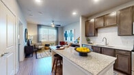 This single-floor residence offers a thoughtfully designed open-concept layout that seamlessly connects the kitchen, dining, and living areas. The kitchen is a standout feature, equipped with rich dark wood cabinetry, stainless steel appliances including a refrigerator, range, microwave, and dishwasher, complemented by granite countertops and a classic white subway tile backsplash. A center island with bar seating provides additional prep space and a casual dining option. Light wood-style flooring runs throughout the main living areas, enhancing the bright and airy atmosphere created by large windows fitted with blinds and sheer drapes. The living room offers a comfortable, welcoming layout with ample natural light and ceiling fan. Two well-proportioned bedrooms each feature large windows, ceiling fans, and plush carpeting, offering restful retreats. The bathroom is generously sized, showcasing a granite-topped vanity with dark wood cabinetry, a soaking tub with subway tile surround, and direct access to a spacious walk-in closet outfitted with built-in shelving and hanging rods. Recessed lighting throughout the unit adds a clean, modern touch to this cohesive and functional living space.