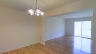 This single-floor space offers a clean, open layout designed to maximize both comfort and functionality. The interior is finished with warm-toned hardwood flooring that runs throughout, lending a sense of continuity and natural warmth to the living areas. Crisp white walls provide a neutral backdrop that enhances the brightness of the space, allowing light to reflect freely across each room.

A standout feature of the dining area is the classic multi-arm chandelier, suspended from the ceiling and adding a touch of traditional elegance to the space. The open-plan design seamlessly connects the dining area to the adjacent living space, creating a flowing layout that feels both spacious and inviting.

Natural light plays an important role in the ambiance of this space, with a glass exterior door visible in the background allowing daylight to filter in and illuminate the interior. The smooth white ceilings complement the light hardwood floors, reinforcing the airy, uncluttered feel throughout.

Overall, this space presents a well-maintained, move-in ready environment with timeless finishes, an intuitive layout, and an inviting atmosphere well-suited for everyday living.