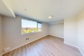 Located at 1221 NE 180th St in Shoreline, WA, this two-bedroom, one-bathroom residence offers a well-designed single-floor layout with a clean, modern aesthetic. Light wood-style luxury vinyl plank flooring runs throughout the main living areas and hallways, lending a cohesive and contemporary feel to the space.

A central hallway connects all rooms efficiently, featuring recessed lighting and sliding doors that maximize space. The spacious primary bedroom is generously sized, bathed in natural light through a large picture window that frames elevated treetop and neighborhood views — a standout feature of the home. The second bedroom is similarly appointed, with its own large window offering comparable outdoor views and ample room for flexible use.

The bathroom is finished in a clean, minimalist style with light flooring, white walls, a dark-toned vanity with a sink, and accessibility-friendly grab bars. A dedicated closet provides practical storage, complete with wire shelving and carpeted flooring. The second bedroom also features carpet, offering a softer feel distinct from the rest of the unit.

Throughout the space, neutral warm-toned walls, recessed and flush-mount lighting, and consistent finishes create a bright and welcoming ambiance. The overall layout is functional and thoughtfully organized, making efficient use of the available square footage.