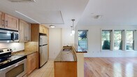 Located at 87 New St in Cambridge, MA, this two-bedroom, one-bathroom residence offers a well-organized single-floor layout designed for comfortable everyday living. The open-concept kitchen and living area serves as the heart of the home, where warm hardwood floors extend through the living space while tile flooring grounds the kitchen. The kitchen is fully equipped with stainless steel appliances, including a refrigerator, electric range, and microwave, complemented by rich granite countertops, light wood cabinetry, and a peninsula with pendant lighting that provides both additional workspace and a casual dining option. Multiple windows flood the living area with natural light and offer pleasant views of the greenery outside. The spacious primary bedroom features soft carpeting and windows overlooking the yard, creating a calm and private retreat. The second bedroom is similarly carpeted and well-lit with natural light through its windows. The bathroom includes a combination tub and shower, tile flooring, and a vanity with ample storage. Neutral wall tones throughout the residence provide a clean, versatile backdrop. The lush outdoor surroundings visible from multiple rooms add a refreshing sense of nature to this Cambridge home.