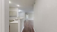 This single-story residence offers a thoughtfully designed layout spanning two bedrooms and two bathrooms. Rich, dark hardwood-style flooring flows consistently throughout the home, creating a cohesive and polished aesthetic in every room.

The open living room serves as the centerpiece of the home, featuring crown molding, a ceiling fan, a classic fireplace with a white surround, and a window that invites natural light. The space connects seamlessly to the kitchen and dining area, enhancing the overall sense of openness.

The kitchen is equipped with sage-toned cabinetry, white appliances including a refrigerator, electric range, and over-the-range microwave, along with a light-colored countertop peninsula that doubles as a breakfast bar. A utility room provides additional functional space within the home.

The primary bedroom is generously sized, featuring a ceiling fan, a sliding glass door leading to an outdoor patio with views of surrounding greenery, and dedicated closet space. The second bedroom also includes a ceiling fan, natural light from a window, and its own closet.

Both bathrooms maintain the home's clean aesthetic. One features a walk-in glass-enclosed shower with marble-style tile surround, while the other offers a full soaking tub and shower combination, both with sage cabinetry and wood-style flooring.
