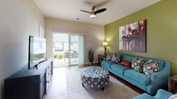 This single-story residence is thoughtfully designed with an open-concept floor plan that seamlessly connects the main living areas. The kitchen is outfitted with rich dark wood cabinetry, granite-style countertops, black appliances including a refrigerator, range, and built-in microwave, and a central island with bar seating — ideal for casual dining or meal prep. Wood-look flooring flows throughout the main living spaces, lending a warm, cohesive aesthetic.

Adjacent to the kitchen, a dedicated dining area accommodates a full-sized table and chairs, accented by decorative wall art and a ceiling-mounted light fixture. The living room is generously proportioned, featuring a bold green accent wall, a ceiling fan, and a sliding glass door that opens to a private patio with outdoor seating, allowing natural light to pour into the space.

The bedrooms offer comfortable retreats with carpeted flooring, large windows with natural light, and ample closet storage. The bathroom features granite-style countertops, a wide vanity with an oversized mirror, and clean, neutral finishes. Throughout the residence, neutral wall tones are complemented by colorful décor, creating a vibrant yet welcoming atmosphere.