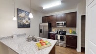This single-story residence offers a cohesive, thoughtfully designed interior with neutral tones and quality finishes throughout. The kitchen serves as a central highlight, featuring rich dark-espresso cabinetry, light granite countertops, and a full suite of stainless steel appliances including a French door refrigerator, electric range, over-the-range microwave, and dishwasher. A peninsula with a double basin sink and pendant lighting extends toward the living area, creating an open, connected layout. Wood-look flooring runs through the kitchen and main living spaces, adding warmth and continuity.

The living room is comfortable and inviting, finished with dark hardwood-style flooring, a ceiling fan, and access to an exterior door. A separate dining area accommodates a round table beneath a pendant light fixture and includes a double-door closet for additional storage. The bedroom features plush carpeting, a ceiling fan, and a window with natural light. The bathroom is finished with large-format tile flooring, a dark vanity with granite countertop, an undermount sink, and a full-width mirror, maintaining the consistent aesthetic found throughout the residence.