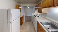 Located at 2294 Zink Rd. in Fairborn, Ohio, this single-floor unit offers a straightforward and functional layout spread across several well-defined rooms. The interior is finished with warm beige carpeting throughout the living and bedroom areas, providing a consistent and comfortable feel underfoot. Crisp white walls and standard ceilings give each room a clean, neutral backdrop well-suited for personalization.

The living area is generously proportioned, featuring a wide bank of windows fitted with horizontal blinds that allow ample natural light to fill the space. Baseboard heating units are present throughout, ensuring efficient climate control across all rooms. Several of the carpeted rooms also feature wall-mounted air conditioning units, providing year-round comfort.

The kitchen is a functional galley-style space equipped with warm wood-toned cabinetry, white countertops, a white electric range, and a full-size refrigerator. Tile flooring and a ceiling fan with light fixture complete the kitchen area, which opens directly into an adjacent carpeted room. Multiple rooms throughout the unit include closet space and additional doorways connecting to hallways and other areas. The overall layout, as revealed by the dollhouse view, is a well-organized, multi-room floor plan designed for practical everyday living.