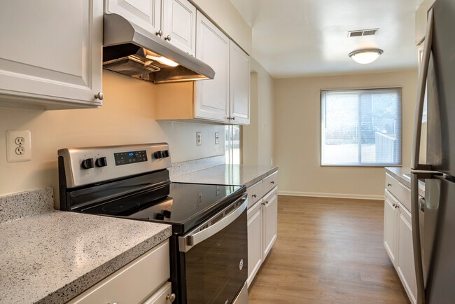 Renovated Package I kitchen featuring stainless steel appliances, white cabinetry, grey laminated countertops, and hard surface flooring - Tysons Crossing