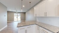 Located at 6842 Main St in Buffalo, NY, this well-appointed two-story home offers three bedrooms and two bathrooms across two thoughtfully designed floors. The main level features an open-concept kitchen and living area highlighted by white shaker cabinetry, granite countertops, pendant lighting, and stainless steel appliances. A kitchen peninsula provides additional workspace and seating, while large sliding glass doors in the living room flood the space with natural light and provide direct access to the outdoors. Light-toned hardwood-style flooring flows throughout the main level, complementing the neutral gray palette and clean-lined aesthetic. Two entrances and connecting hallways add convenience and flow to the layout. Upstairs, the second floor houses the three bedrooms, including a generously sized primary bedroom, as well as two full bathrooms. The bedrooms feature plush carpeting and soft neutral walls, with select rooms benefiting from windows that invite natural light and outdoor views. The bathrooms are finished with granite-topped vanities and light wood-look flooring, maintaining a consistent modern aesthetic throughout. A staircase connects both levels seamlessly. The overall ambiance is clean, contemporary, and move-in ready.