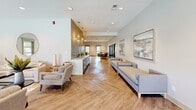 Located at 400 Mallard Creek Rd in St. Matthews, Kentucky, this thoughtfully designed community clubhouse offers a generous, open-concept layout spread across a single floor. The interior is anchored by stunning herringbone-patterned hardwood flooring that flows seamlessly throughout, lending warmth and sophistication to the entire space.

The main lounge area is furnished with neutral-toned sofas, accent chairs, and a round wall mirror, all set beneath recessed lighting that creates a bright, welcoming atmosphere. A decorative accent wall with pendant lighting separates the lounge from a dedicated dining area, which features a round marble-top table surrounded by modern upholstered chairs. Floor-to-ceiling windows in the dining area frame direct views of the outdoor pool and lush landscaping, flooding the space with natural light.

A secondary seating nook, highlighted by vaulted ceilings and multiple windows, offers a quieter retreat with views of the surrounding greenery. Glass-panel sliding doors provide additional privacy options and connect various zones of the space. The overall design palette of soft whites, warm taupes, and natural wood tones creates a cohesive, contemporary aesthetic that is both functional and inviting for residents and guests alike.
