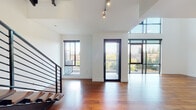 This contemporary multi-floor residence showcases a sophisticated modern design characterized by clean lines, an open layout, and an abundance of natural light. Rich hardwood flooring flows throughout the main living areas, complemented by crisp white walls and sleek black-framed windows and railings that create a striking visual contrast.

The main living level impresses with soaring vaulted ceilings and expansive floor-to-ceiling glazing, including a glass door that opens to a balcony overlooking lush treetop views. A bold open-riser staircase with a black steel railing serves as both a functional and architectural centerpiece, connecting all three floors seamlessly.

The kitchen is a standout feature, outfitted with two-tone cabinetry in dark walnut and light gloss finishes, a generous waterfall-edge island, stainless steel appliances, and pendant lighting. A second galley-style kitchen space offers additional functionality with ample cabinetry and built-in appliances.

The upper level includes a spacious bedroom with hardwood floors and windows framing city skyline views. The ensuite bathroom is elegantly appointed with large-format tile, a raised soaking tub, glass partitions, a vanity with undermount sink, and an expansive mirror. Additional bathroom facilities are provided on other levels. The multi-floor layout provides a well-organized, versatile living environment with a refined urban aesthetic throughout.